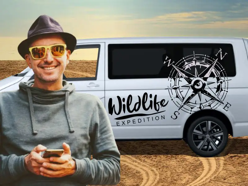 Glücklicher Mann mit Sonnenbrille am weißen Camping-Bus VW T6 mit großem Kompass Windrose Motiv in Schwarz